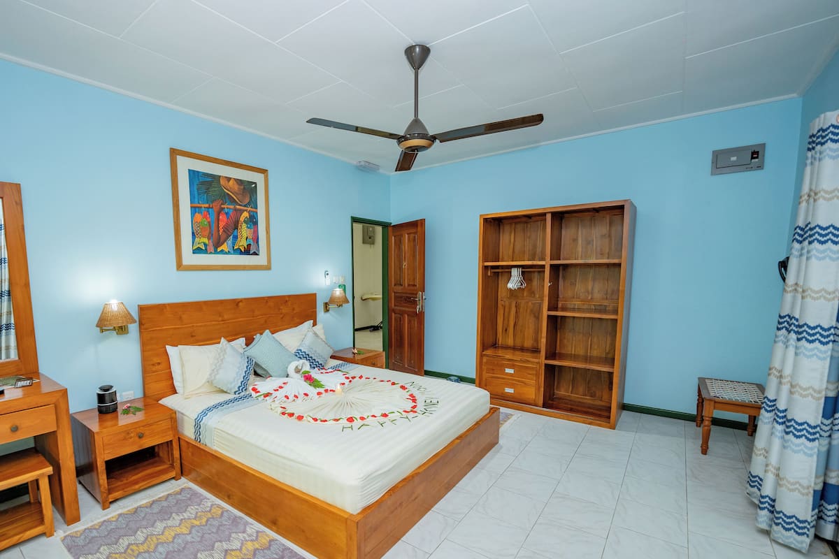 Un dormitorio con una cama de madera, un ventilador de techo, un armario de madera, una mesita de noche y una lámpara de pared.