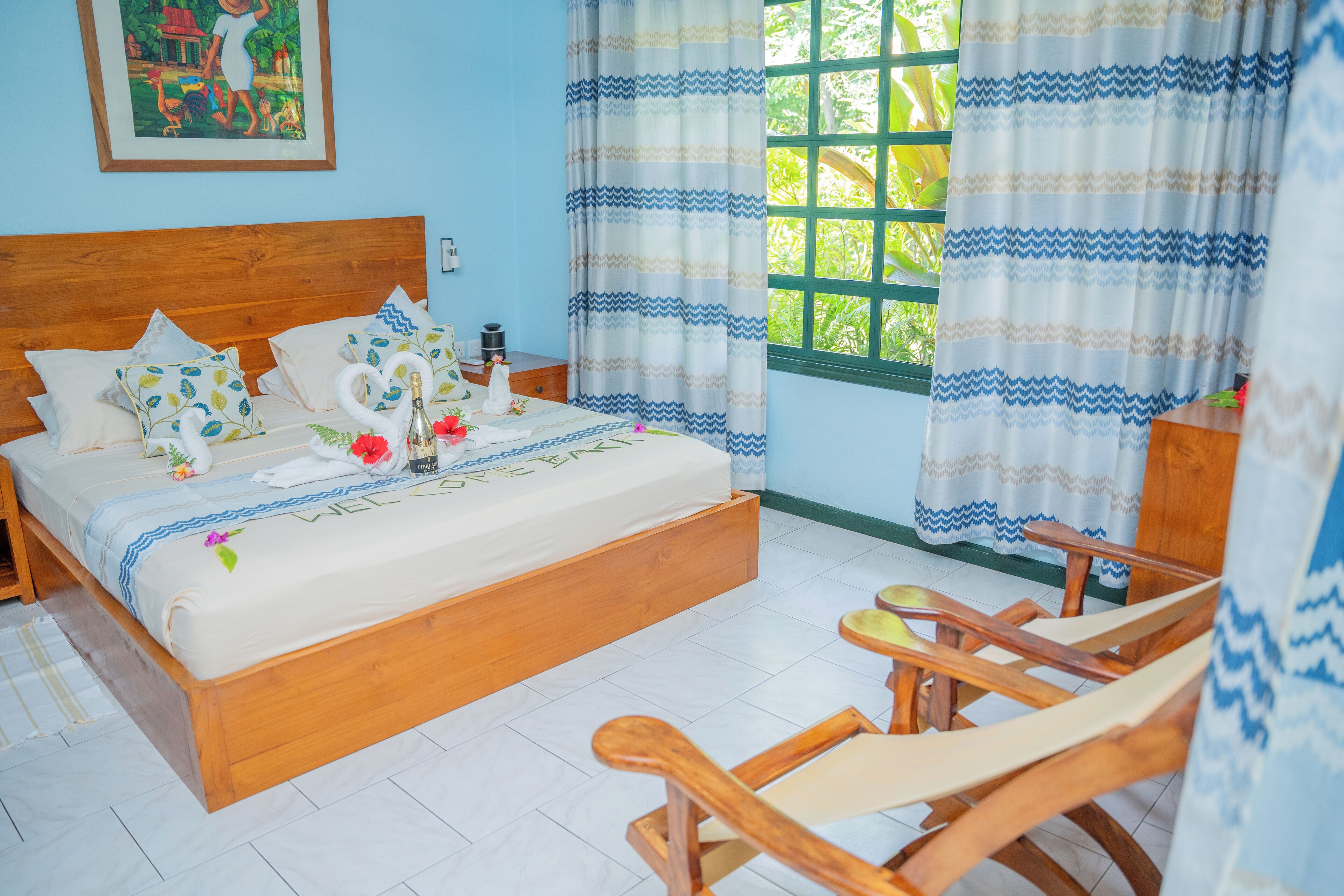 Una cama bien hecha con almohadas y un adorno con forma de corazón, una mecedora de madera y una ventana con cortinas.