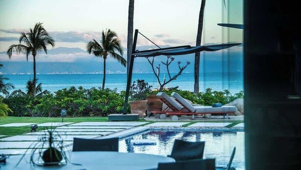 Ein Poolbereich mit Liegestühlen, einem Tisch und Blick auf den Ozean.