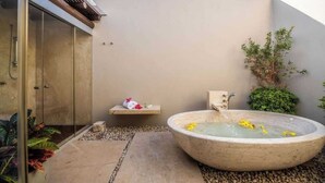 Ein Wellnessbereich mit einer großen Steinbadewanne, einer Holztür und einem kleinen Ablagebereich für Handtücher.