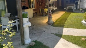 Une maison en bois dotée d’un patio comprenant une table et des chaises, un petit jardin et un espace salon couvert.