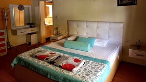 Une chambre à coucher avec un grand lit, une table de chevet, un miroir, une armoire et une salle de bain visible à travers une porte ouverte.