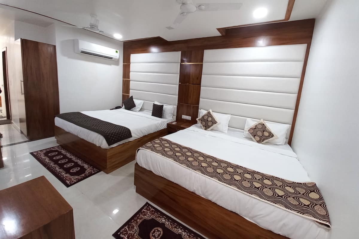 Une chambre d’hôtel avec deux lits, une tête de lit en bois, un ventilateur de plafond et un appareil de climatisation.