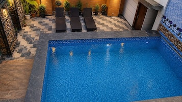 An indoor swimming pool with a tiled floor, lounge chairs, and potted plants.
