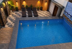 An indoor swimming pool with a tiled floor, lounge chairs, and potted plants. - HOTEL The Rich Grand (Agra)