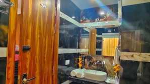 A bathroom with a wooden door, a sink with toiletries, a mirror, and a marble backsplash. - HOTEL The Rich Grand (Agra)