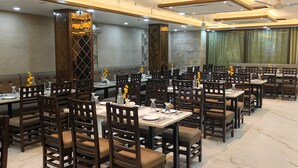 A restaurant with multiple dining tables and chairs, ceiling fans, and recessed lighting. - HOTEL The Rich Grand (Agra)