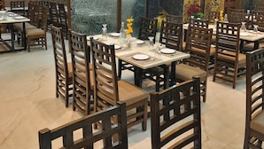 A restaurant with wooden chairs and tables, decorative panels, and a ceiling fan. - HOTEL The Rich Grand (Agra)