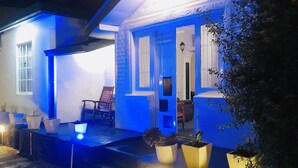 Un bâtiment à la façade bleue, avec une porte bien visible et une chaise placée à l’extérieur.