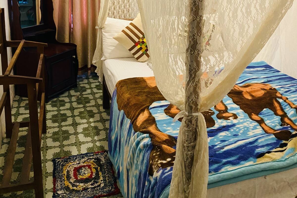 Ein Schlafzimmer mit einem Bett, das mit einer blau-braunen Decke bezogen ist, einem hölzernen Nachttisch, einem kleinen Tisch und einem dekorativen Teppich.