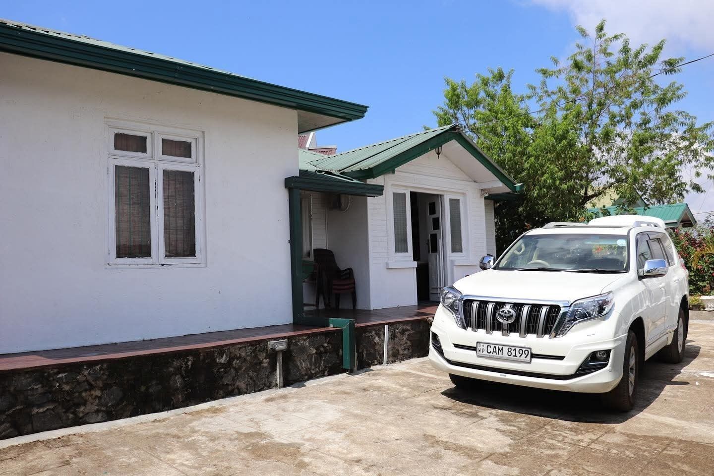 A white SUV parked in front of a house with a green roof and white walls.