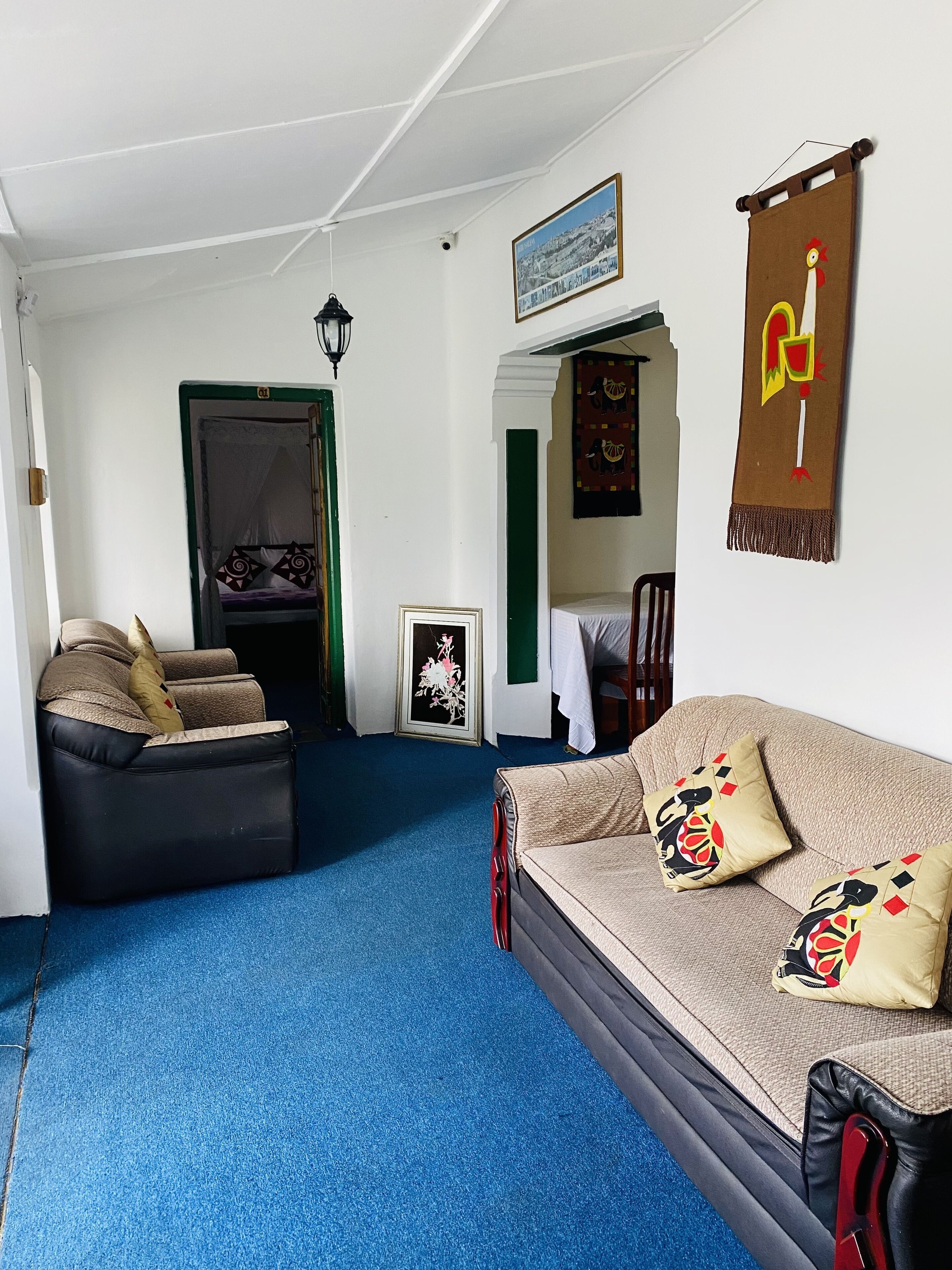 Une pièce avec un tapis bleu, un canapé orné de coussins à motifs, une chaise noire et un lit avec une tête de lit blanche.