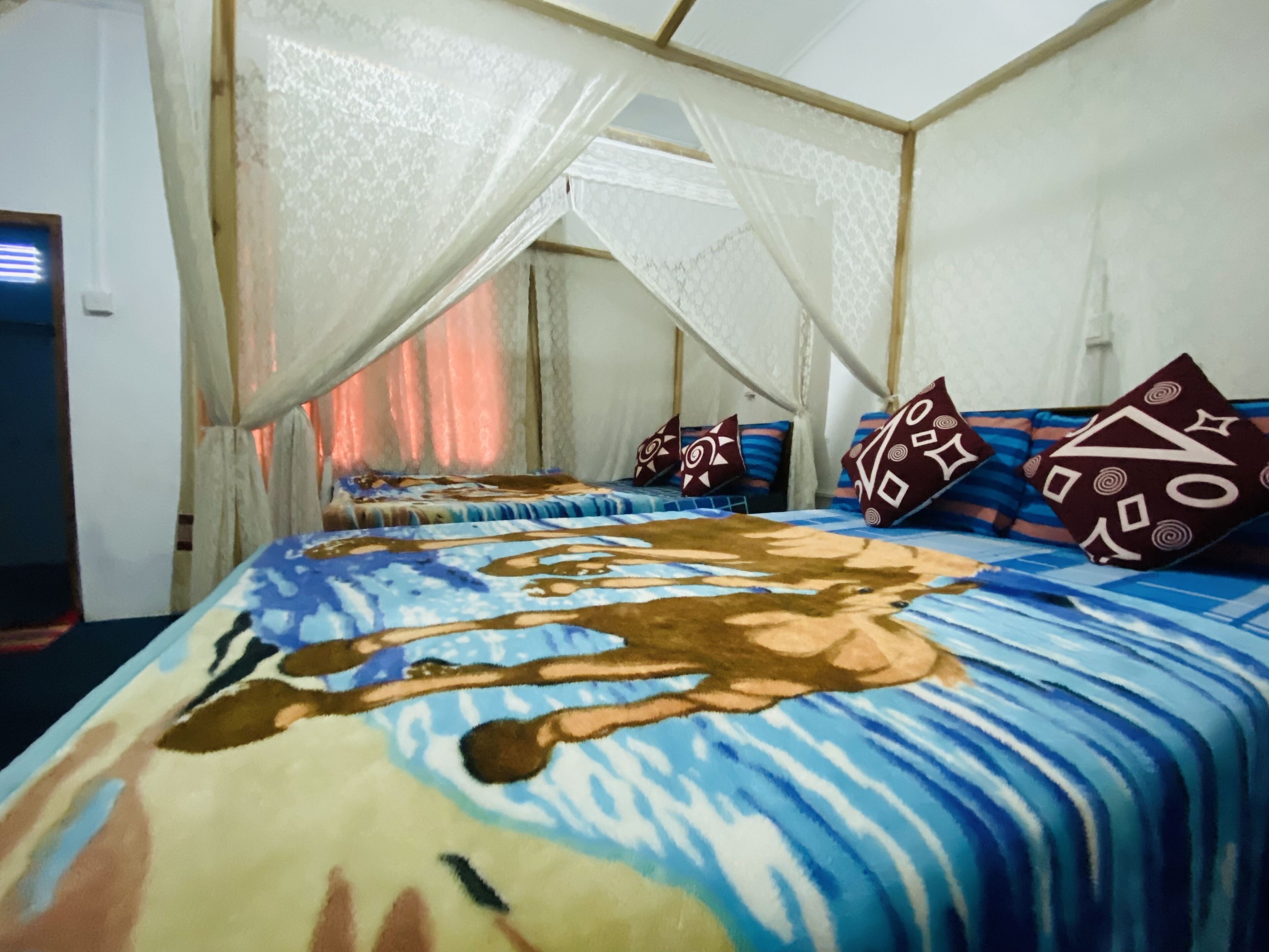 A room with a bed covered in a colorful blanket, a canopy bed, and patterned pillows.