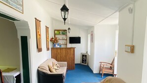 Un grand espace de vie agrémenté d’une moquette bleue, d’un comptoir d’accueil en bois, d’un canapé, d’un fauteuil et d’un téléviseur fixé au mur.