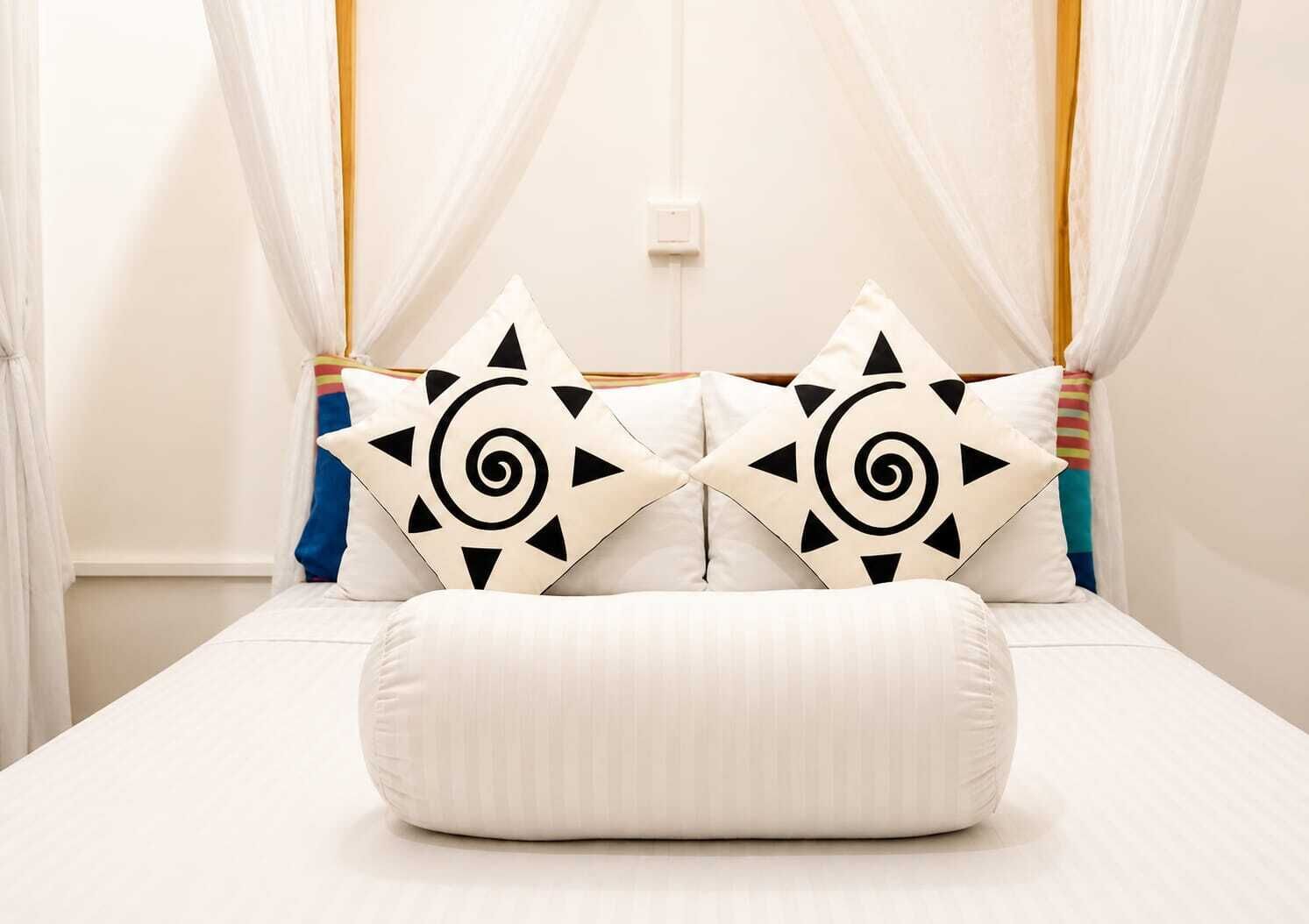 A bed with a canopy, two decorative pillows with geometric patterns, and a plain white wall.