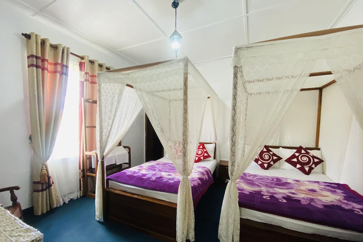 Ein Zimmer mit zwei Betten, jedes mit Baldachin, und einem hölzernen Stuhl.