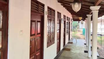 A covered corridor with wooden doors and columns, a white plastic chair, and a hanging light fixture.
