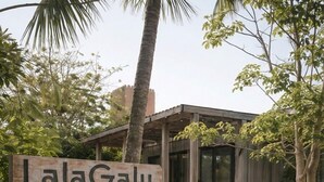 Un edificio con un letrero que dice 'LalaGalu', rodeado de un jardín ajardinado con senderos de grava y diversas plantas.