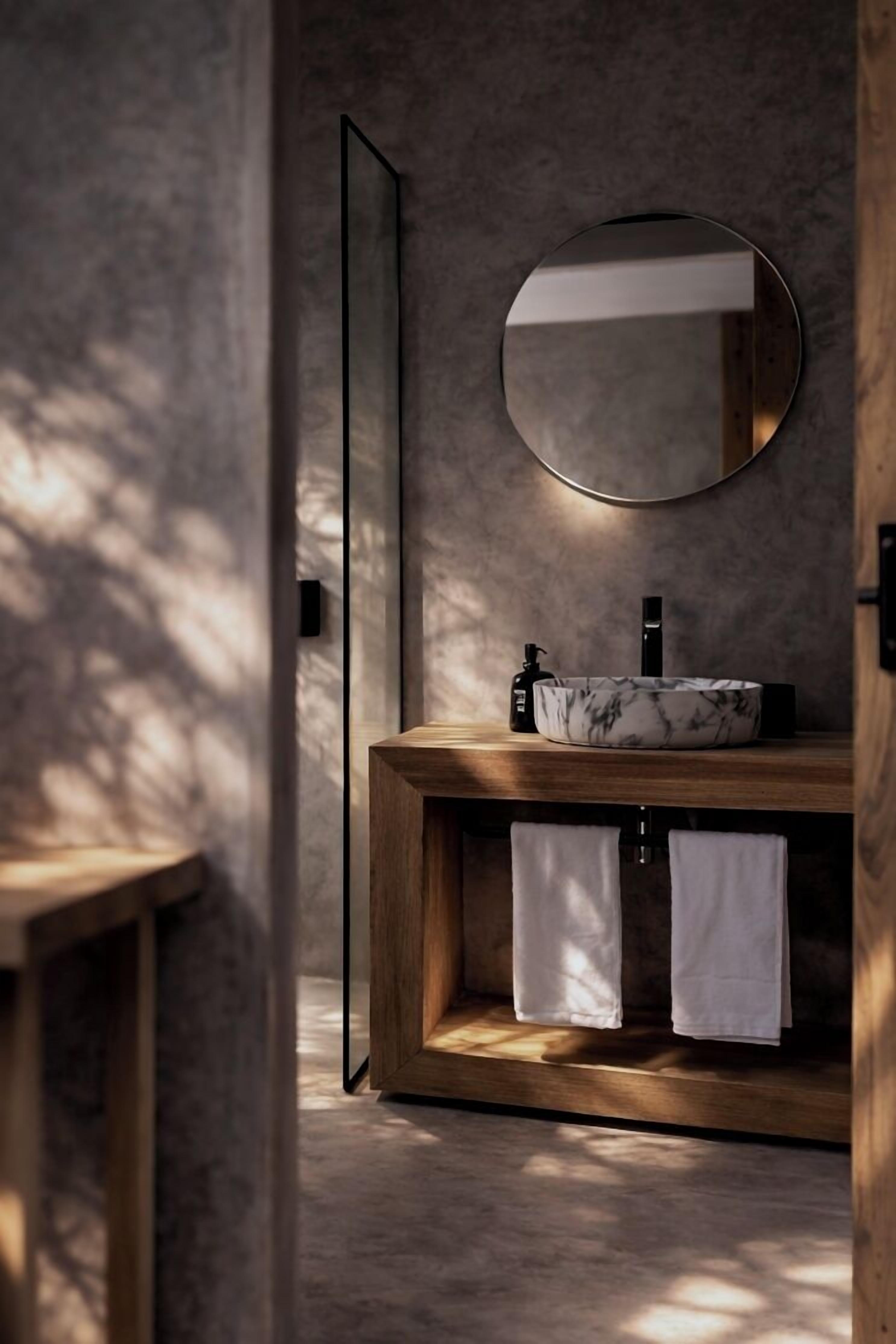 A modern bathroom with a wooden vanity, a round mirror, and two white towels.