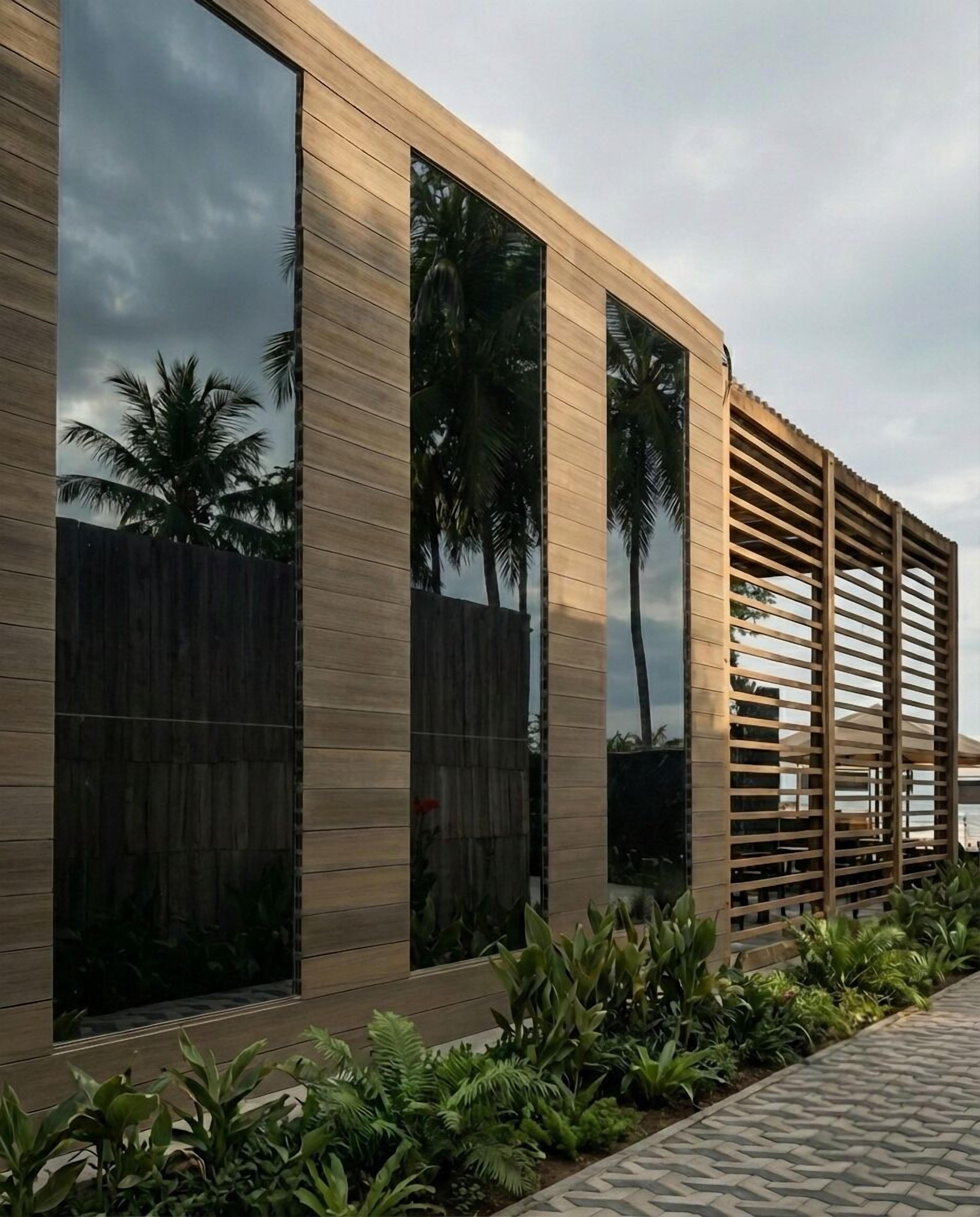 Un edificio moderno con amplios ventanales, fachada de madera y un jardín ajardinado.