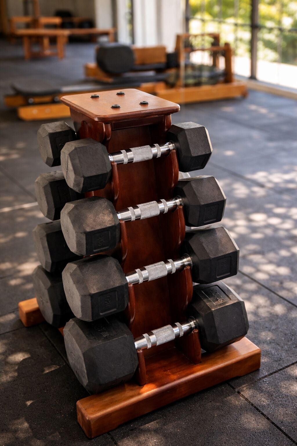 A stack of black dumbbells on a wooden stand with a metal bar in the center.