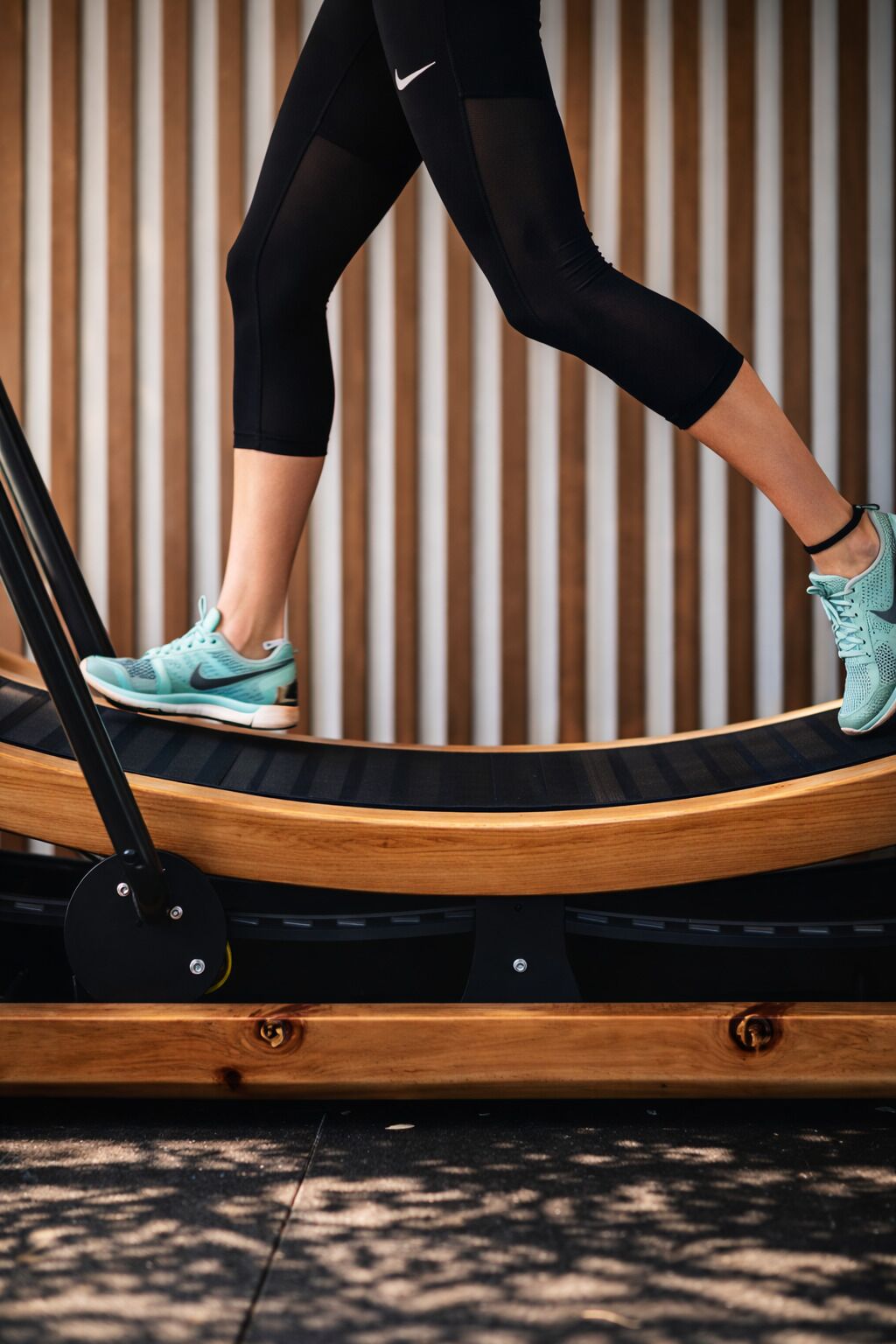 A person using a treadmill with a wooden frame and a black base, set against a wooden wall with vertical slats.