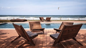 Una terraza de madera con sillones de descanso y una piscina con vista al océano.