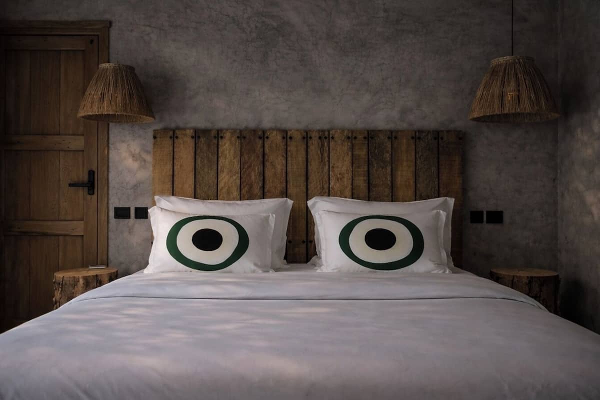 Una cama con cabecera de madera, dos lámparas de noche y un par de almohadas con diseños circulares.