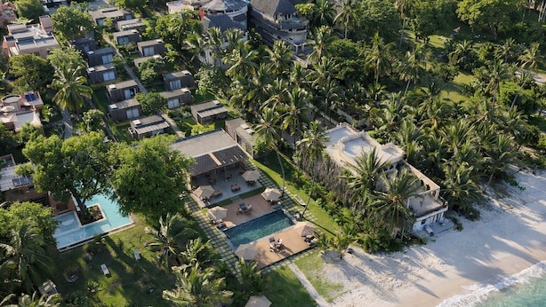 Vista aérea de un resort con varias cabañas, un área de piscina central y una playa.