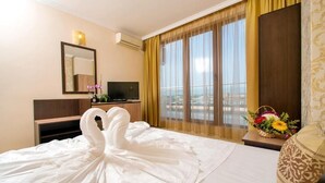 Une chambre d’hôtel avec un lit, une télévision, un miroir, une fenêtre avec des rideaux et une vue sur la ville.