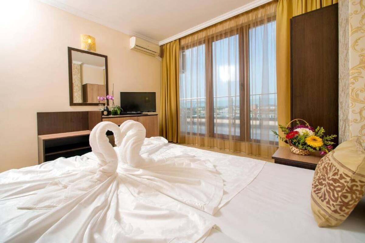 Habitación de hotel con cama, televisión, espejo, ventana con cortinas y vista a la ciudad.