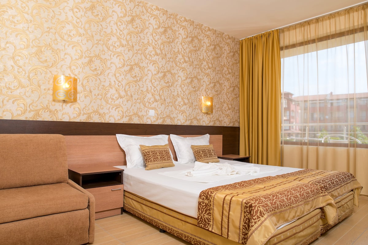 Una habitación de hotel con una cama grande, un sofá, una mesita de noche y dos apliques de pared.