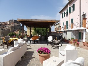 Patio esterno con mobili in vimini, zona relax coperta e piante in vaso.