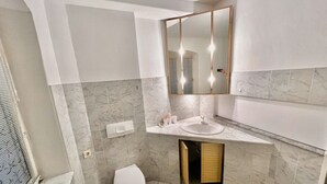 Un bagno moderno con pavimento in marmo, un water bianco, un lavandino con uno specchio sopra e un interruttore a parete.