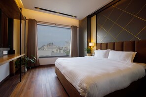 Ein Hotelzimmer mit einem großen Bett, Holzboden, einem Vorhangfenster, einer Pflanze und Blick auf die Stadt.