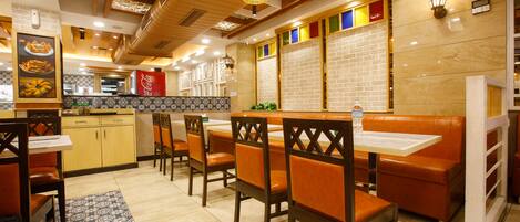 A restaurant interior with booths, wooden chairs, a tiled floor, and a brick wall.