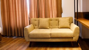A beige sofa with four cushions in a room with wooden flooring and a curtain in the background. - Sangam City Hotel (Kathmandu)