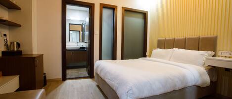 A modern hotel room with a large bed, a desk, and a vanity with a mirror.
