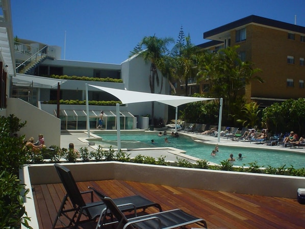 Relax by the pool surrounded by lounge chairs and umbrellas, with a staircase and balcony nearby.