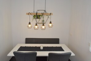Un espace repas avec une table blanche, des chaises foncées et un luminaire hexagonal agrémenté de plantes.