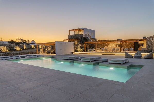 Un espace piscine extérieur moderne, avec des chaises longues et un bâtiment en pierre en arrière-plan.