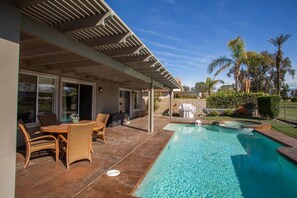 A covered outdoor area with a pool, patio furniture, and a view of the surrounding landscape.