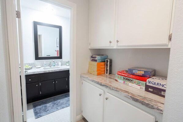 A bathroom with a white sink, dark cabinets, and a mirror. There are boxes of games on the countertop.