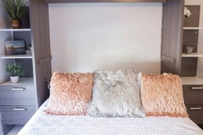A bed with three fluffy pillows and a white textured bedspread.