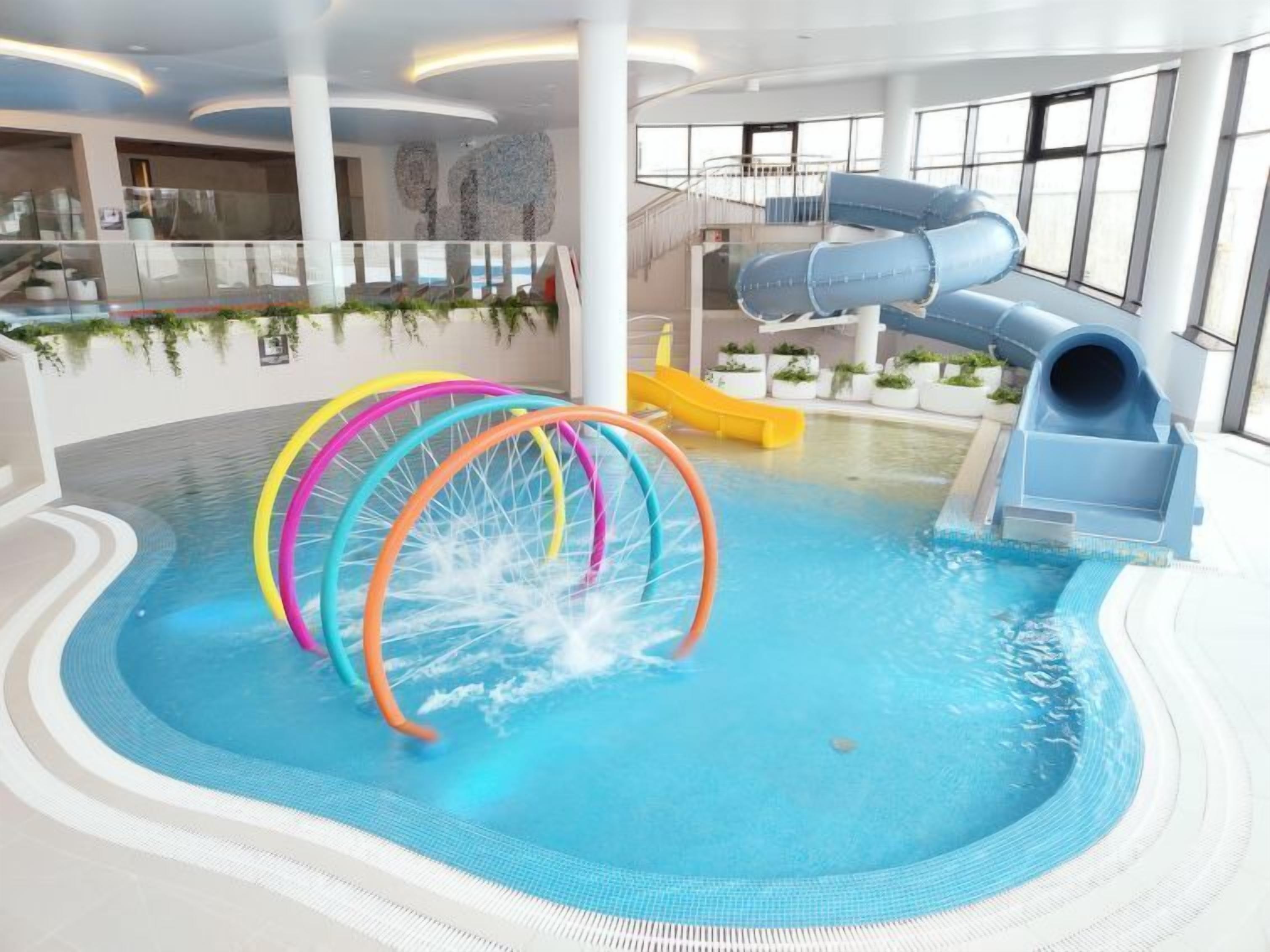 Piscina interna com escorregador e argolas coloridas.