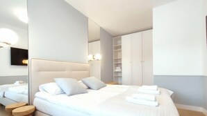 Quarto moderno com uma cama grande, uma mesinha de cabeceira, um guarda-roupa e um espelho.