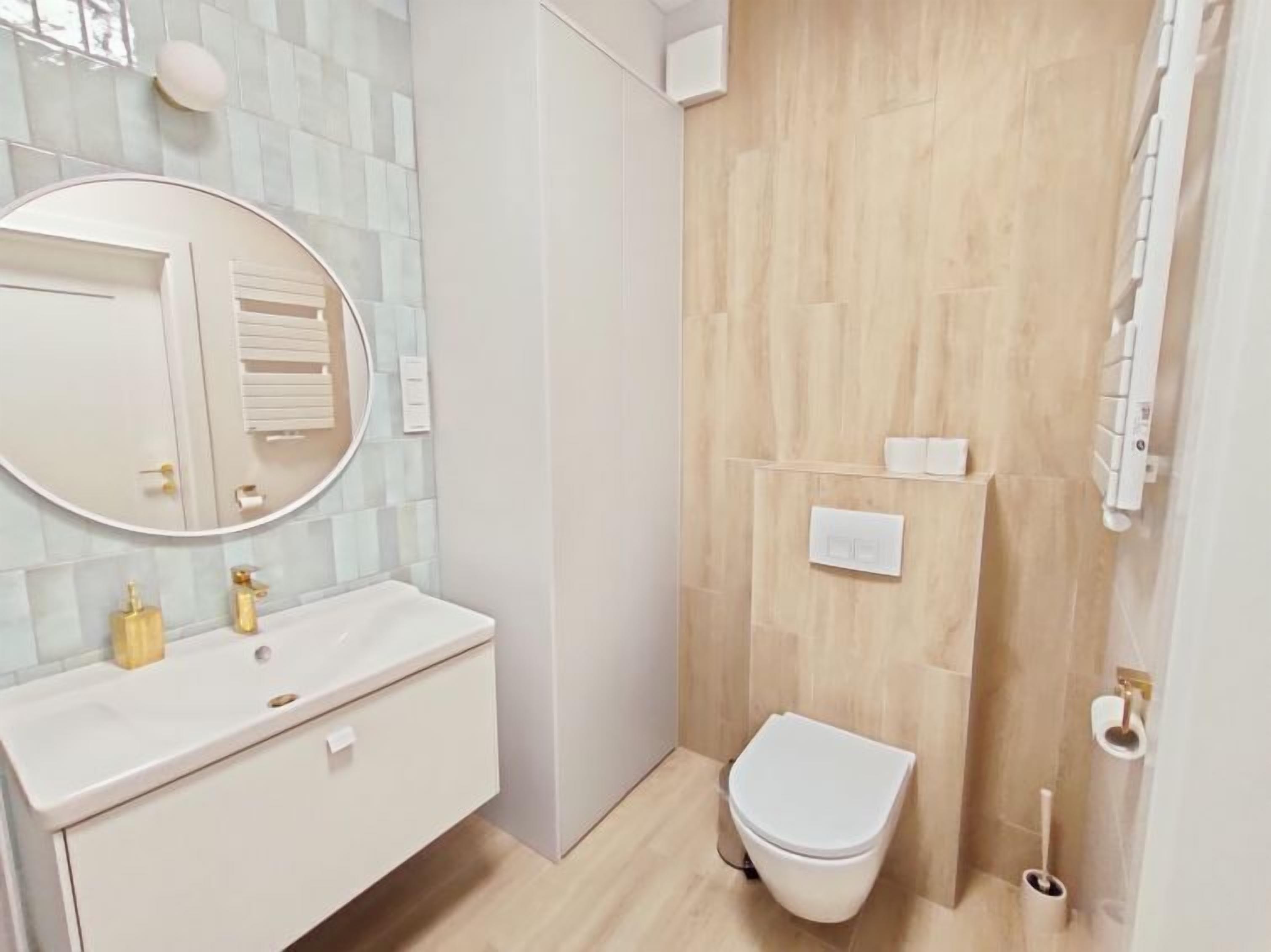 Un baño moderno con un tocador blanco, un espejo redondo, un inodoro y una zona de ducha.