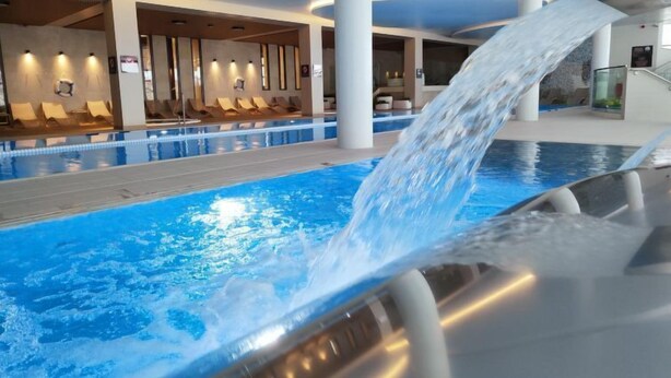 Piscina interior moderna com um recurso aquático, área de descanso e arquitetura contemporânea.