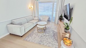 Uma sala de estar moderna com um sofá branco, uma mesa de centro redonda e uma TV fixada na parede.