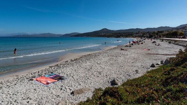 A beach with clear blue water, people sunbathing, and a colorful towel on the sand. - Chez Béatrice et Pascal by Interhome (Lozari)